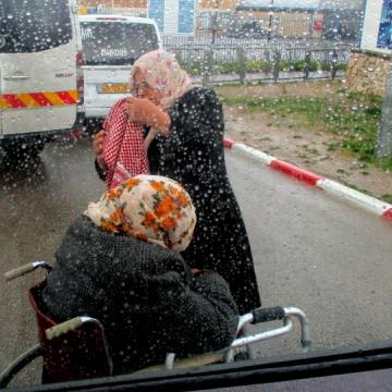 A sick man in a wheelchair next to the van in the rain 